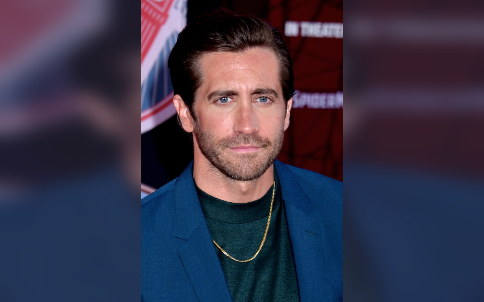 Man with short beard wearing a blue blazer and gold chain at a film premiere