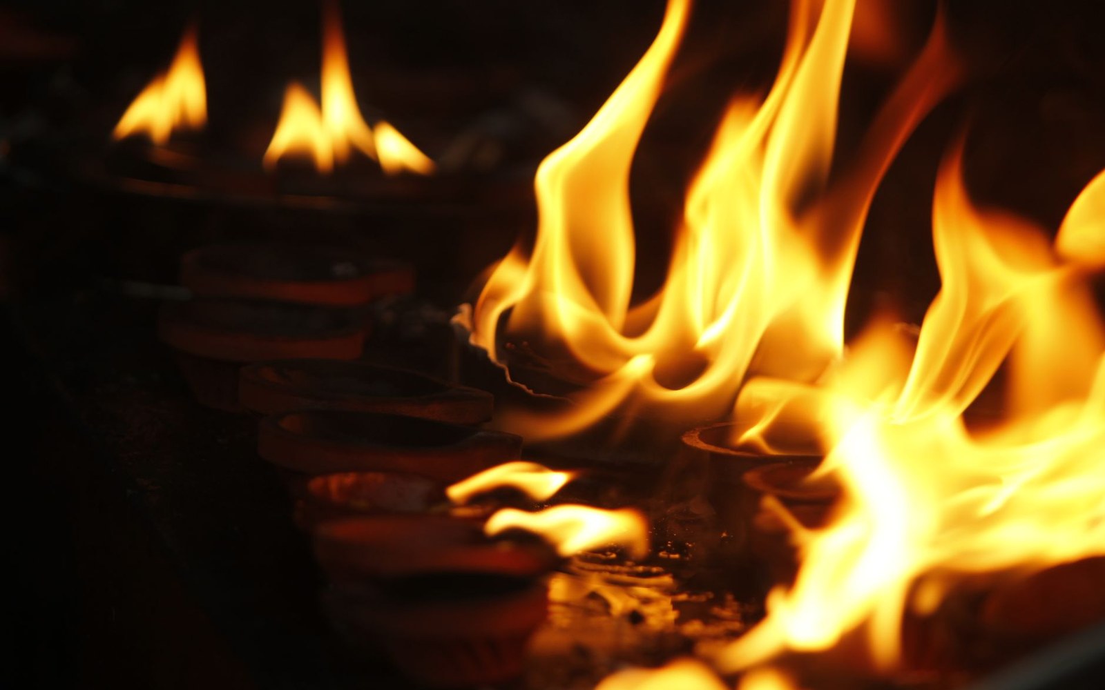 Rows of small clay oil lamps burning with tall flickering flames in darkness