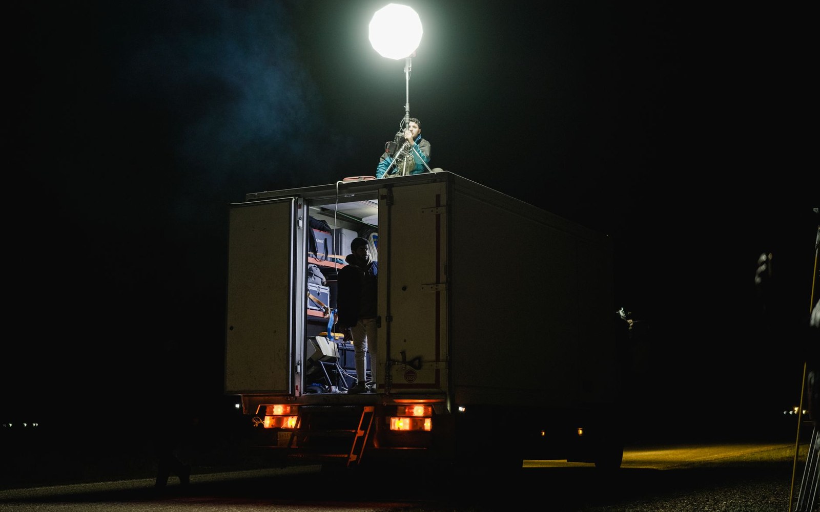 Crew members work atop and inside a truck lit by a large balloon light at night