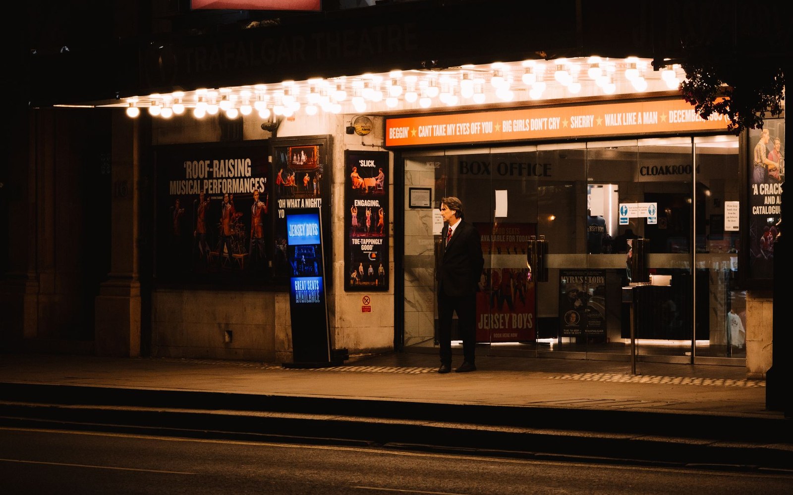 A cinema marquee at night with Jarhead on the letters, wet pavement reflecting the sign, a few adults visible at the box office below